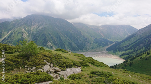 Big Almaty lake located in the mountains of Kazakhstan. It offers views of green grass, flowers, lake, rocks, large mountains and the sky in the clouds. Mountain lake with blue water.