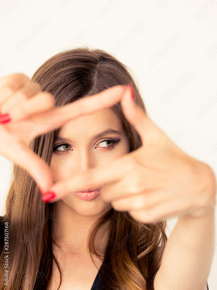 beautiful young girl with perfect skin of the face smiling looks into the camera. close-up portrait with a frame of fingers. positive and emotions beautiful young girl with perfect skin of the face smiling looks into the camera. close-up portrait with a frame of fingers. positive and emotions