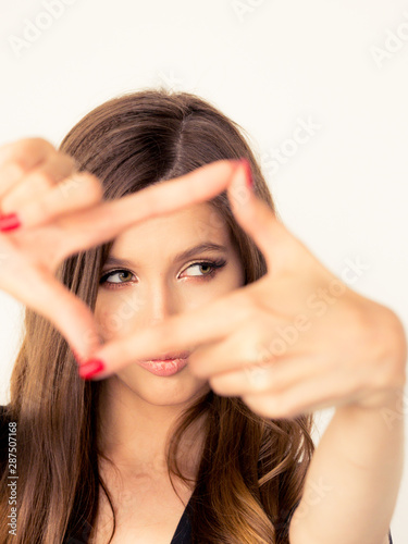 beautiful young girl with perfect skin of the face smiling looks into the camera. close-up portrait with a frame of fingers. positive and emotions