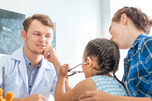 Pediatrician (doctor) man examining little girl patient using a stethoscope in hospital.