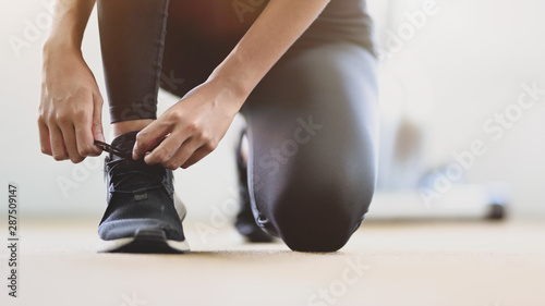 Close-up view of young slim fitness girl doing shoelaces in the sport gym