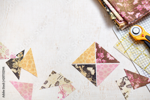 Preparing of triangle pieces of fabrics for sewing quilt blocks, rotary cutter, rule, craft mat, stack of fabrics