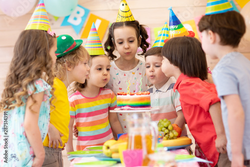 Group of adorable kids 3-5 years gathered around festival table. Children blow out candles on cake. Birthday party for preschoolers