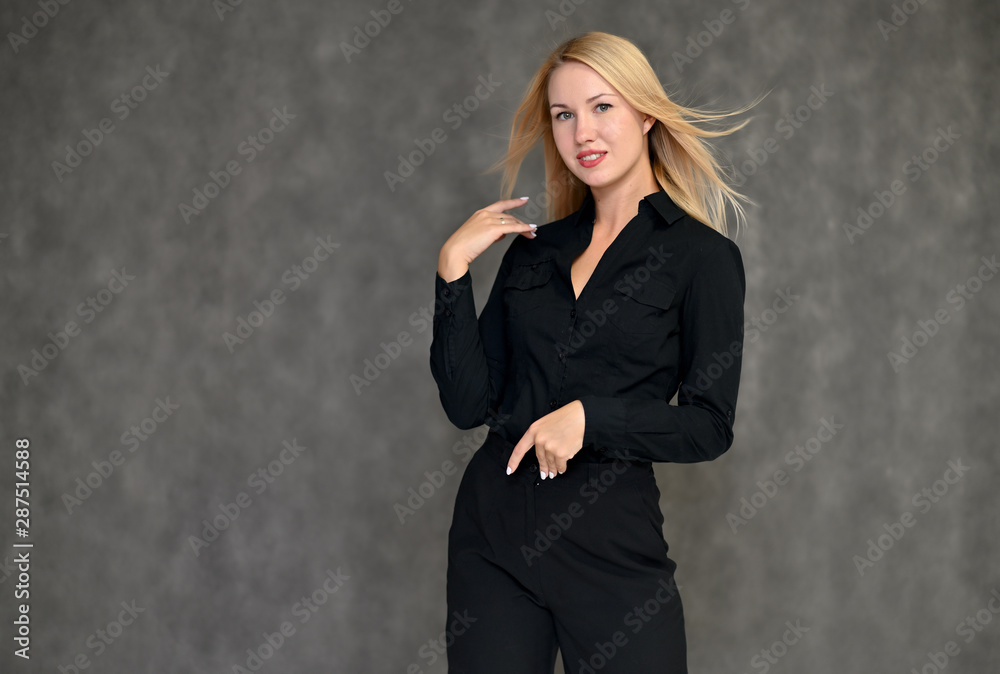 Portrait of a pretty blonde girl in a black suit on a gray background. Beauty, brightness, happiness, business look. Shows different emotions in different poses. Portrait of a pretty blonde girl in a black suit on a gray background. Beauty, brightness, happiness, business look. Shows different emotions in different poses.
