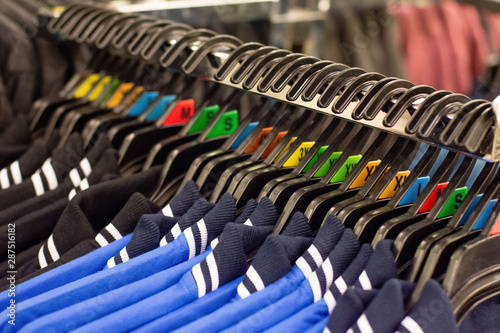 Close up of black and blue polo t-shirts on a clothes rack in retail store. Various sizes index on hangers.