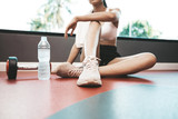 Women sit back and relax after exercise. There is a water bottle and dumbbells.