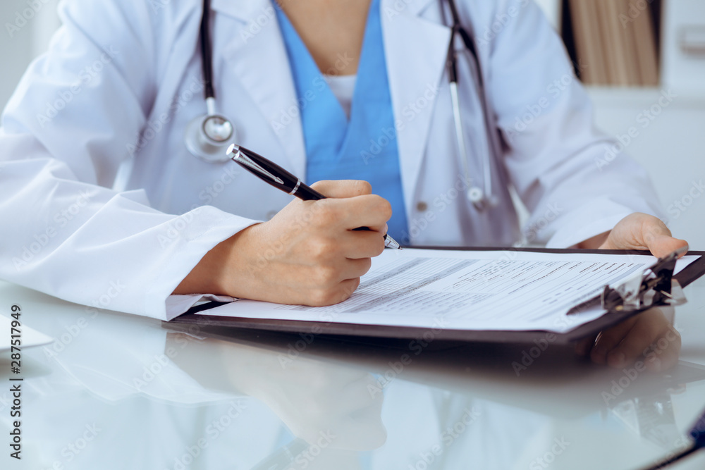Doctor woman filling up medical form while sitting at the table, close-up of hands Doctor woman filling up medical form while sitting at the table, close-up of hands