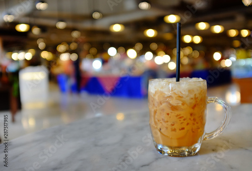 Iced Thai milk tea glass cup on table against department store background.
