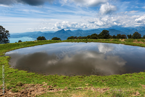 Small pond for livestock with reflections. In the background the Lake Garda and the Alps. Monte Baldo  Verona province  Veneto  Italy  south Europe