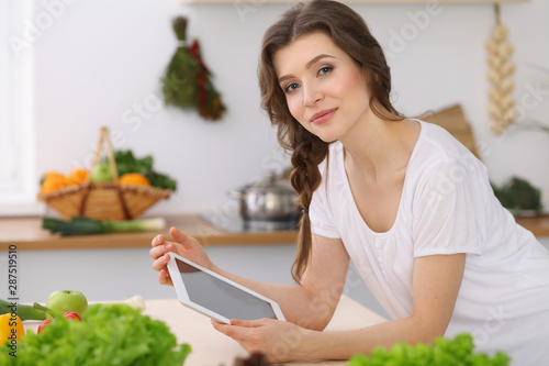 Young woman looking for a new recipe for cooking in a kitchen. Housewife is making online shopping by tablet computer and credit card © rogerphoto