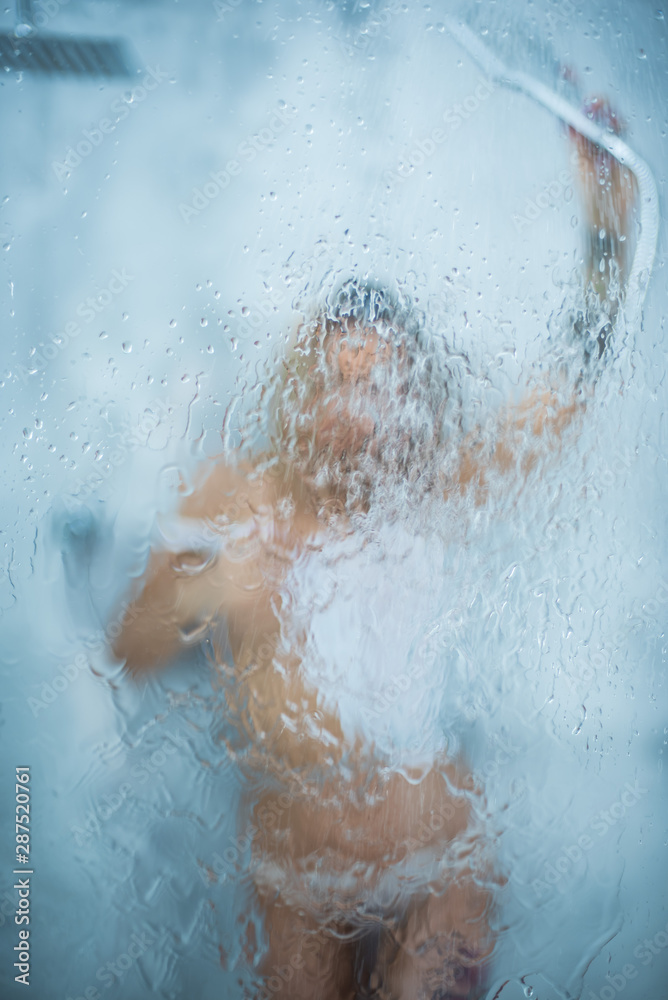 A slender girl in a white wet t-shirt takes a shower, pours water on the