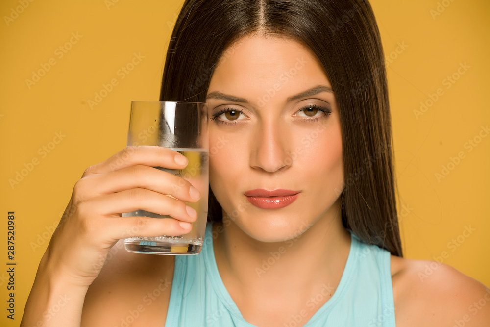 Young woman holding glass of water on yellow background Young woman holding glass of water on yellow background