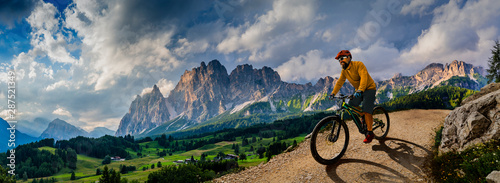 Man cycling on electric bike, rides mountain trail. Man riding on bike in Dolomites mountains landscape. Cycling e-mtb enduro trail track. Outdoor sport activity. photo