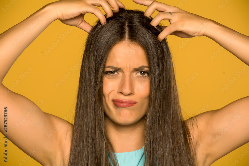 Naklejka premium Beautiful young woman with itchy scalp on yellow background