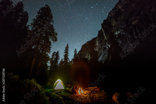 campfire under night sky with star on top of mountain surrounded by forest photo