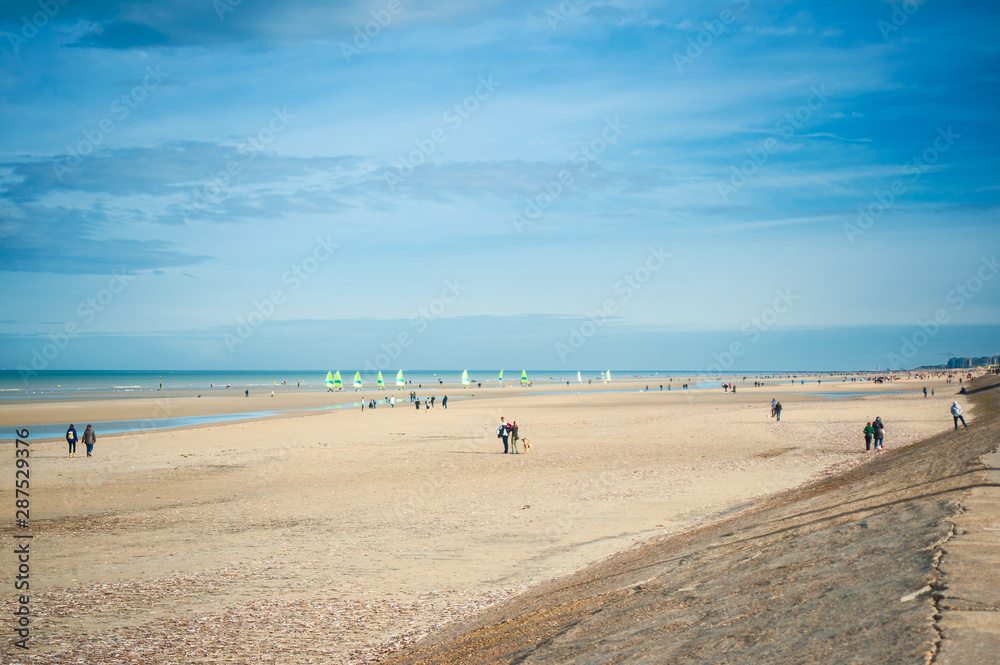 people in autumn at the beach on a sunny day with sailing cars in the background