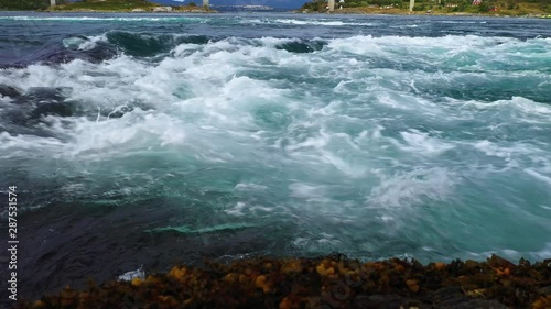 Wide stable low angle shot as harsh water driftin away in a strong tidal current,whie foam dancing on the top of the waves. photo