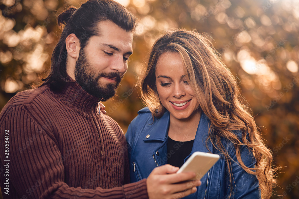 Young couple using cellphone in autumn colored park. Young couple using cellphone in autumn colored park.