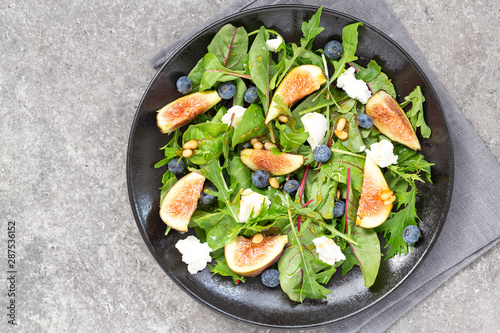 Fig salad with goat cheese, blueberry, with pine nuts and arugula on grey background. Vegetarian food. Top view. 