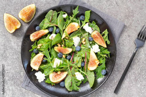 Fig salad with goat cheese, blueberry, with pine nuts and arugula on grey background. Vegetarian food. Top view. 