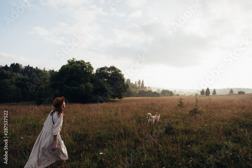 Woman enjoying nature and walking with golden labradore in meadow. Outstretched arms fresh morning air summer Field at sunrise.