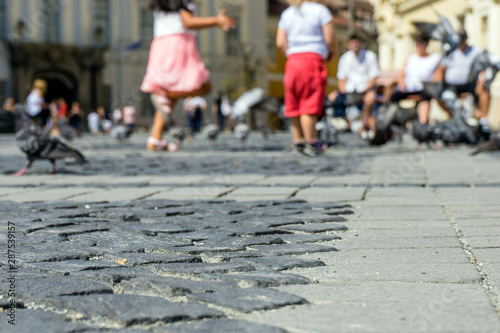 Summer in the city, old cobbled street. Children chase pigeons. View at the sidewalk.