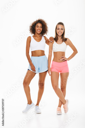 Portrait of two slim multiethnic women wearing sportswear smiling and looking at camera