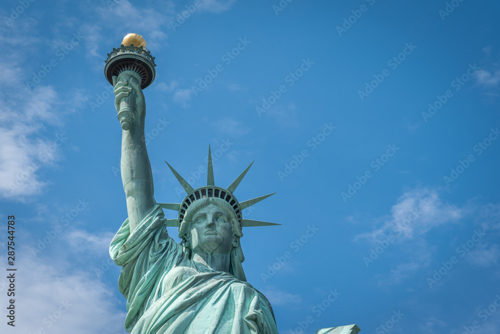 Fototapeta premium Shot of the Statue of Liberty in New York City, Usa. The shot is taken during a beautiful sunny day with a blue sky and white clouds in the background 