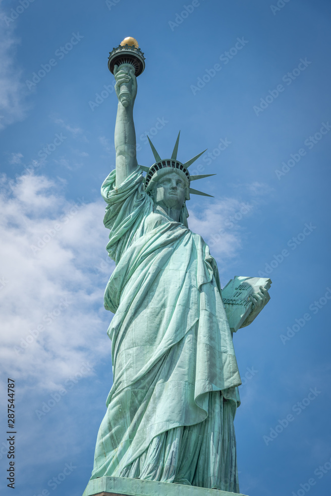Fototapeta premium Shot of the Statue of Liberty in New York City, Usa. The shot is taken during a beautiful sunny day with a blue sky and white clouds in the background 
