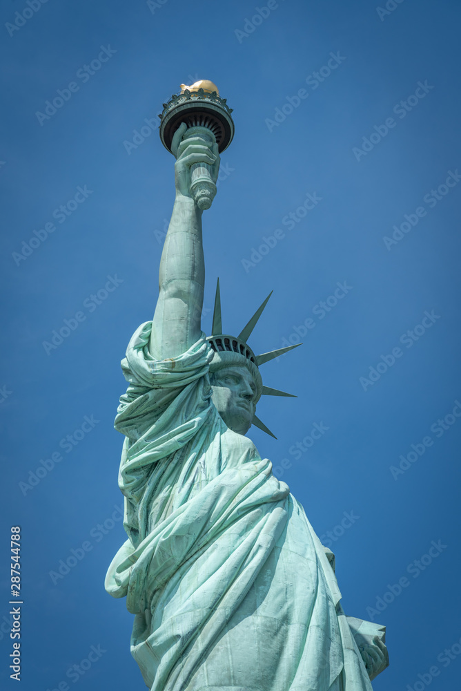 Fototapeta premium Shot of the Statue of Liberty in New York City, Usa. The shot is taken during a beautiful sunny day with a blue sky and white clouds in the background 