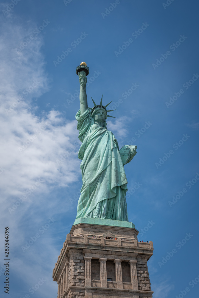 Fototapeta premium Shot of the Statue of Liberty in New York City, Usa. The shot is taken during a beautiful sunny day with a blue sky and white clouds in the background 