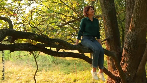 Girl sitting and swinging on a branch of a tree. Young woman in a forest having fun. 