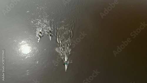 Three kayaks floating on the river, leaving behind a wave in the water reflects the sun. Top view of the drone