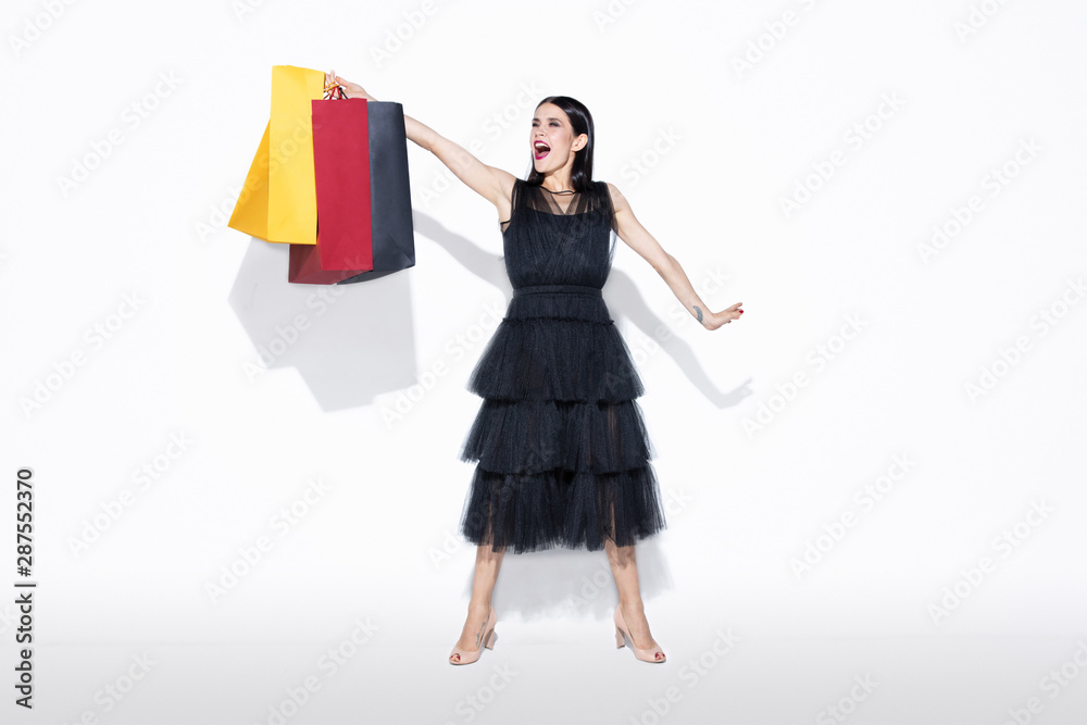 Young brunette woman in black dress shopping on white background. Attractive caucasian female model. Finance, black friday, cyber monday, sales, autumn concept. Copyspace. Screaming, crazy happy. Young brunette woman in black dress shopping on white background. Attractive caucasian female model. Finance, black friday, cyber monday, sales, autumn concept. Copyspace. Screaming, crazy happy.
