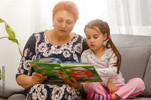 Portrait of a senior woman and a little girl stretched out on a bed reading a book photo