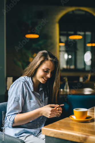 woman using smartphone in cafeteria and drinking coffee