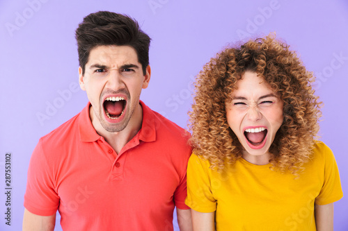 Portrait of emotional young couple man and woman in basic t-shirts screaming together at camera