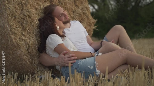 Medium cinematic handheld shot of a romantic mixed race couple leaning on a hay ball wheat spike stack in a field hugging and talking passionately photo