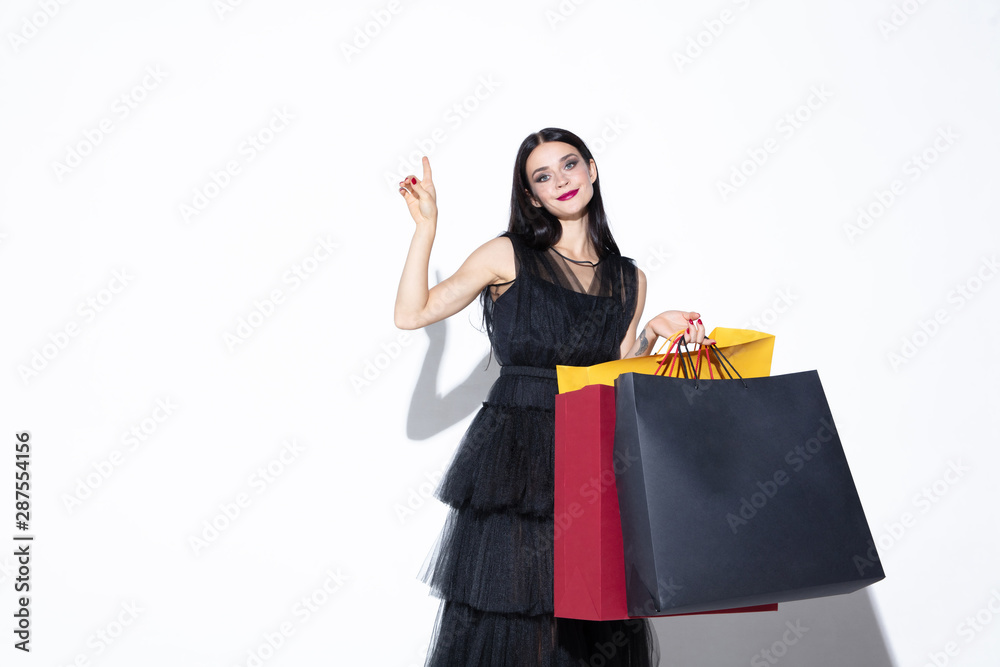 Young brunette woman in black dress shopping on white background. Attractive caucasian female model. Finance, black friday, cyber monday, sales, autumn concept. Copyspace. Pointing, showing. Young brunette woman in black dress shopping on white background. Attractive caucasian female model. Finance, black friday, cyber monday, sales, autumn concept. Copyspace. Pointing, showing.