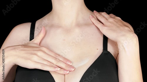 Close-up static medium slow-motion shot of a white lady ribbing oil sensually on her chest while wearing a black bra