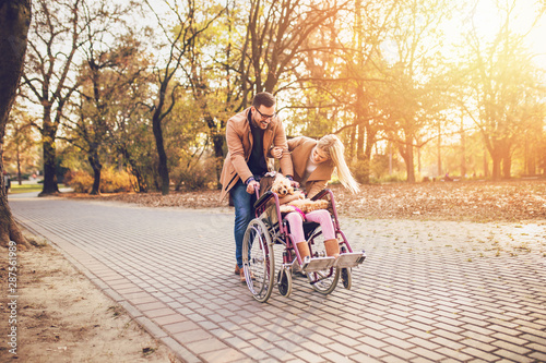 Beautiful disabled girl in wheelchair enjoying with her mother, father and dog outdoors in park.