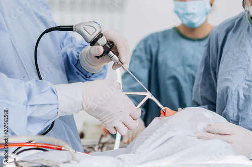 Team of professional Surgeons Performing Invasive Surgery on a Patient in the Hospital Operating Room. Nurse Hands Out Instruments to surgeon, Anesthesiologist Monitors Vitals.