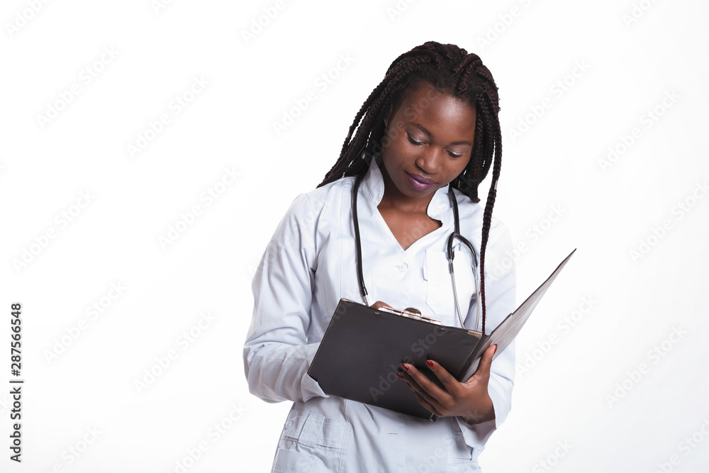 Female american african doctor, nurse woman wearing medical coat with stethoscope write good test results in hospital sheet chart. Happy excited for success medical worker posing on light background Female american african doctor, nurse woman wearing medical coat with stethoscope write good test results in hospital sheet chart. Happy excited for success medical worker posing on light background
