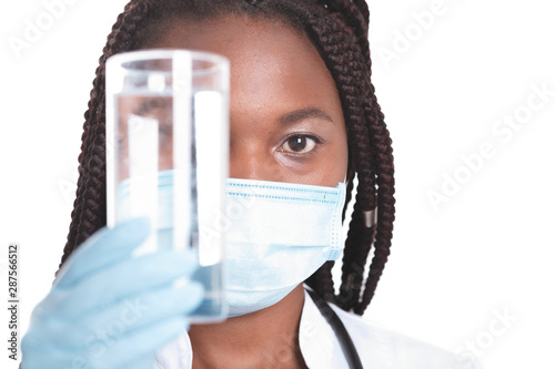 Female american african doctor, nurse woman wearing medical coat with stethoscope, mask and gloves. Doctor holding glass of water. Serious excited for success medical worker posing on light background