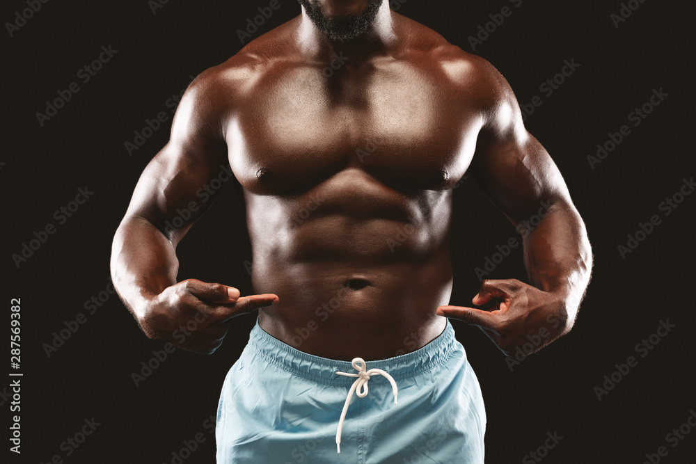 Fototapeta premium Black muscular bodybuilder pointing at his six packs