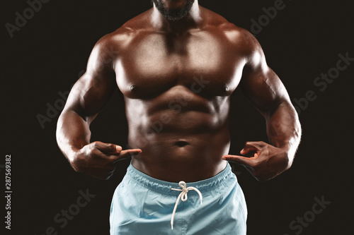 Black muscular bodybuilder pointing at his six packs