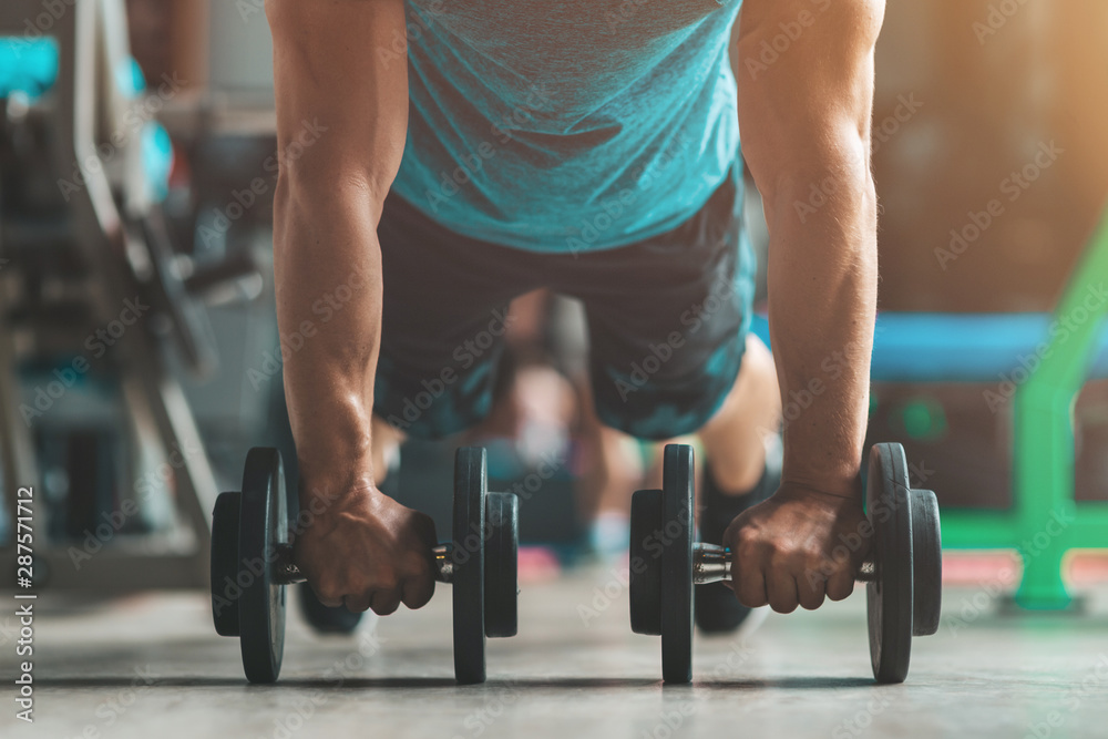 Cropped portrait of adult athlete doing push-ups using dumbbells as part of bodybuilding training. Horizontal shot. Front view Cropped portrait of adult athlete doing push-ups using dumbbells as part of bodybuilding training. Horizontal shot. Front view