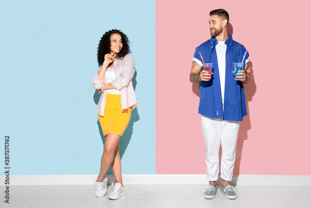 Young emotional caucasian couple in bright casual clothes posing on pink and blue background. Concept of human emotions, facial expession, relations, ad. Man and woman going to drink cocktails. Young emotional caucasian couple in bright casual clothes posing on pink and blue background. Concept of human emotions, facial expession, relations, ad. Man and woman going to drink cocktails.