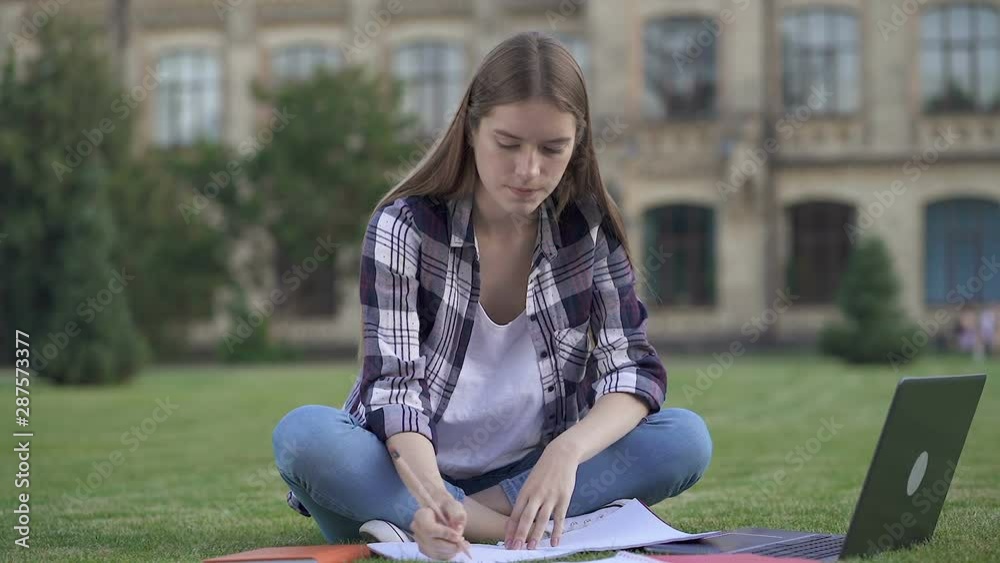 Stressed and unhappy young woman sitting on the grass, working with laptop computer and writing on the paper. Having problem, angry crumpling papaer. Slowmotion.