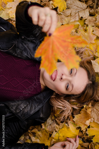 Beautiful woman lying on yellow leaves in park. Leisure time on warm autumn day. Woman showing tongue